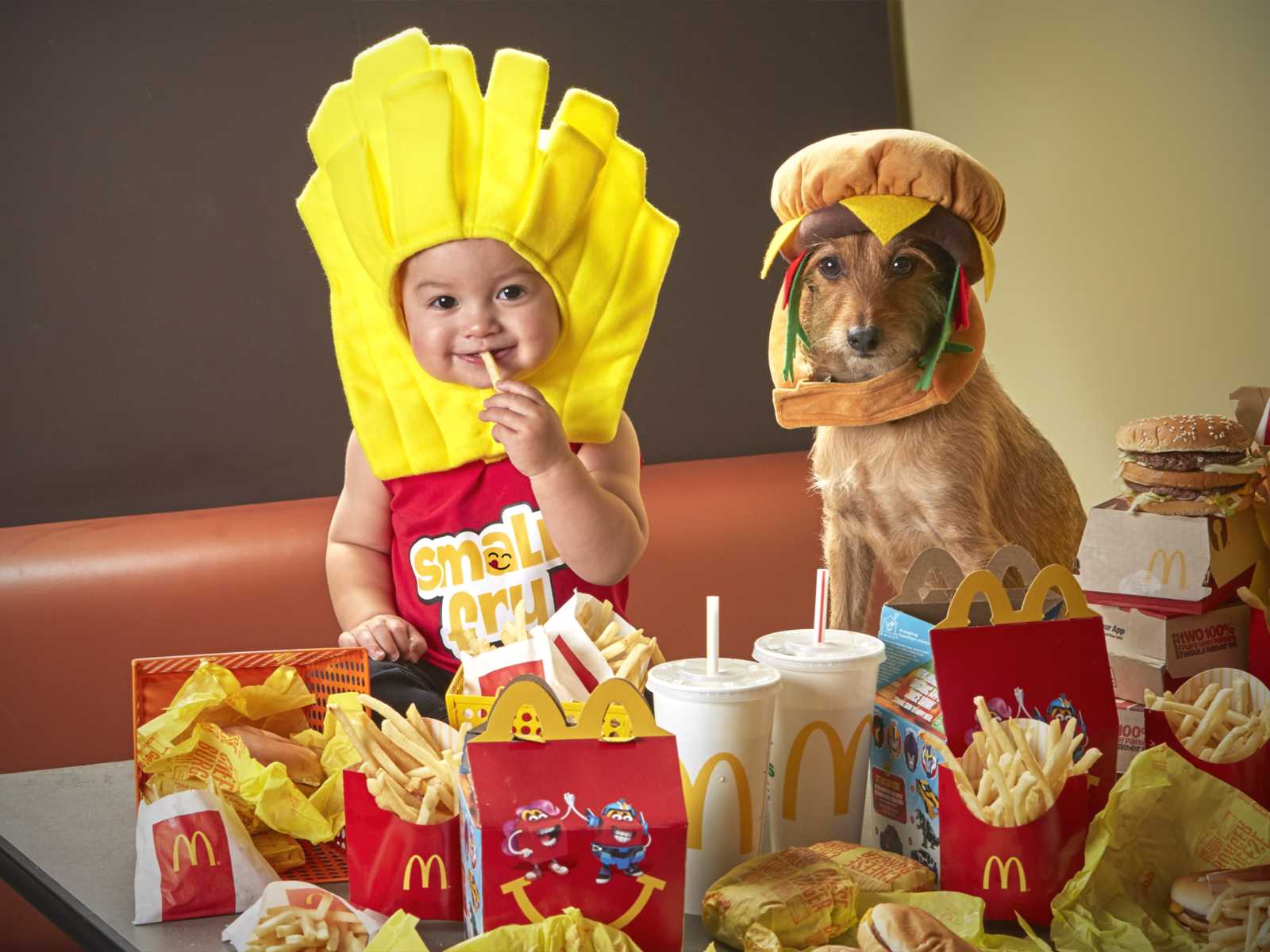 dog in hamburger hat sitting next to baby in fry costume with mcdonald's food in front of them