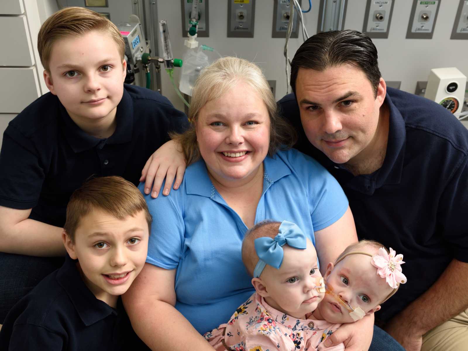 mother sits and holds conjoined baby girls in hospital with husband and other two sons at her side
