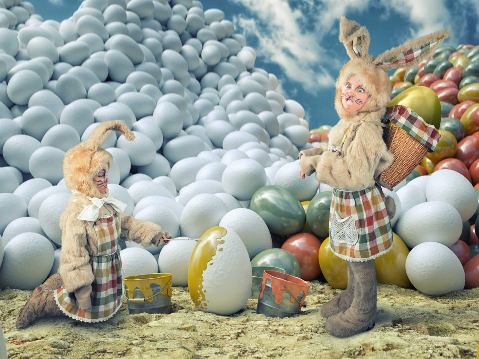 a young girl bunny costume painting white eggs and another girl standing in bunny costume with painted eggs behind her