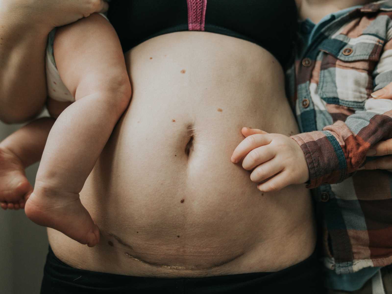 close up of mother's stomach who recently gave birth with gold dust on stretch mark while holding two children