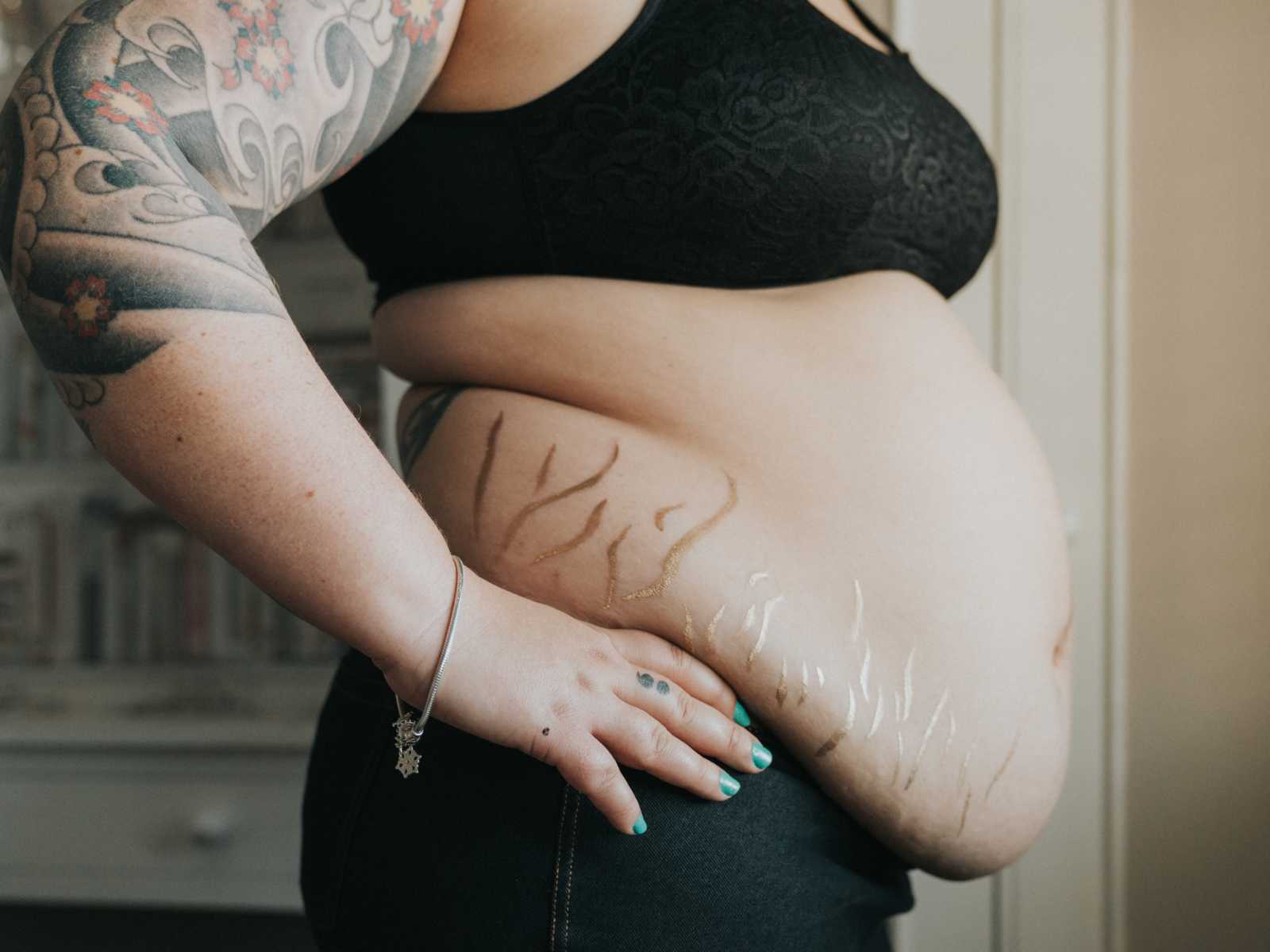 side view of woman's body whose stretch marks are covered in gold dust