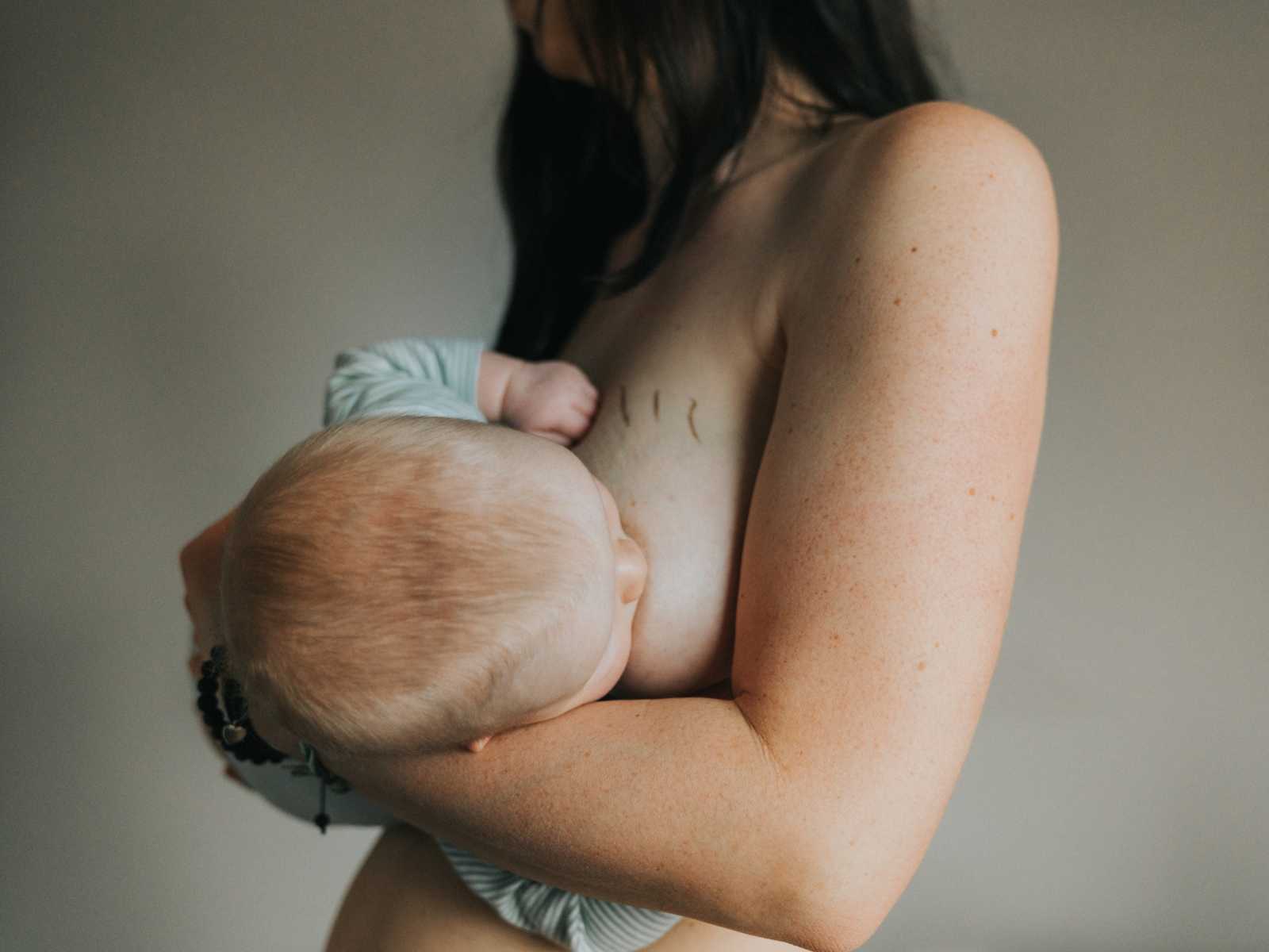 Close up of woman breastfeeding with stretch marks on her breast covered in gold dust