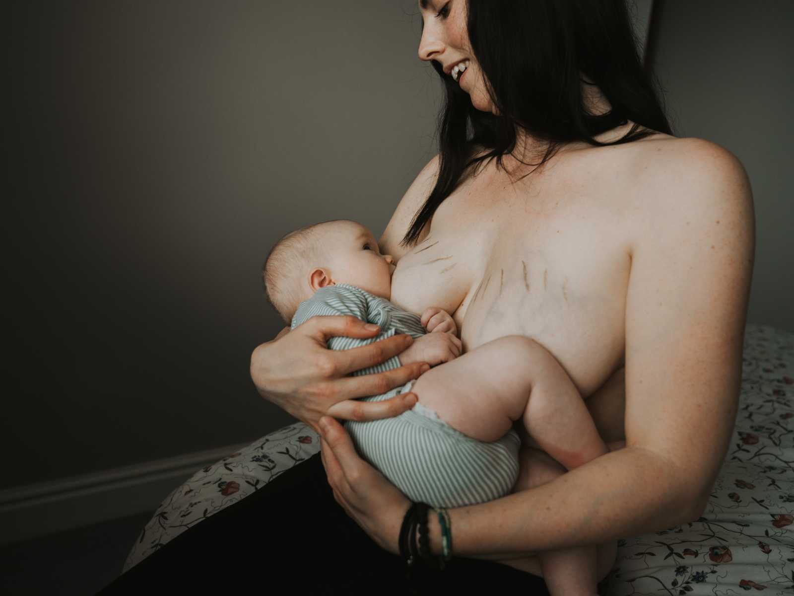 Woman smiling down at baby while breastfeeding with stretch marks in breast covered in gold dust