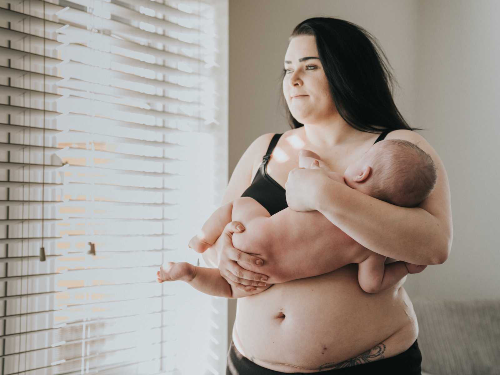 Shirtless mother holds naked baby with stretch marks on stomach covered in gold dust