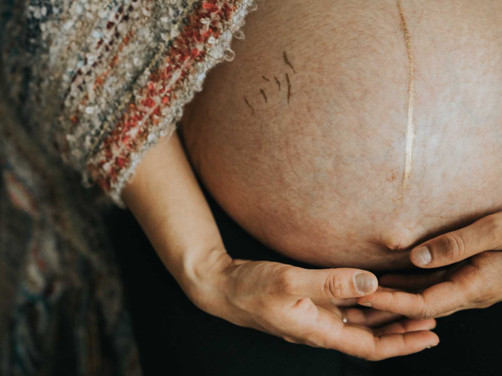 Pregnant woman holds bottom of stretch marked stomach covered in gold