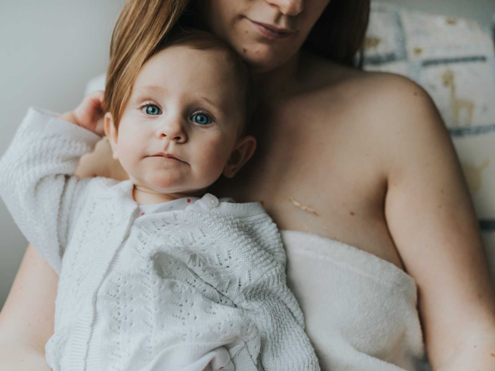 Baby girl sits on mothers lap whose breast has a stretch mark covered in gold dust