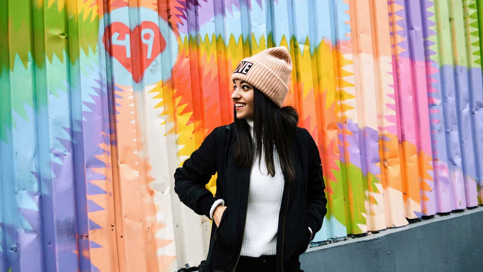 teen stands with hands in pocket smiling over her shoulder in front of colorful mural