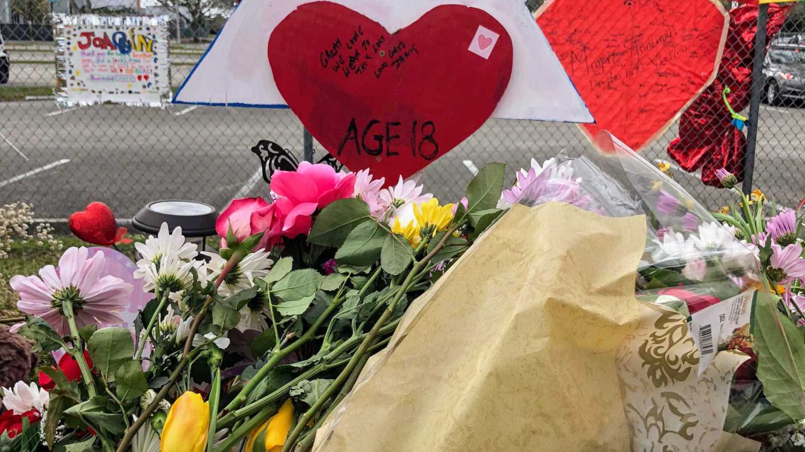 pile of assorted flowers next to fence that has heart poster with "age 18" written on it