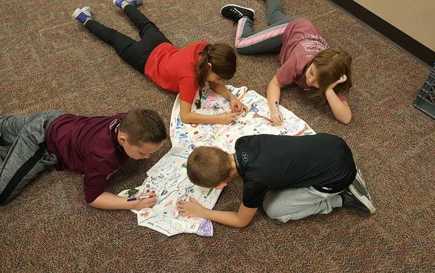 children lying on the floor drawing on teachers white dress