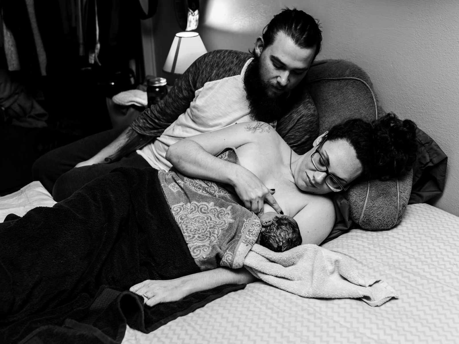 Mother in father of 11 pound newborn baby lie in bed holding the baby