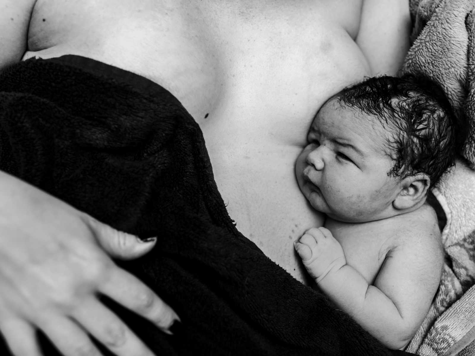 Close up of 11 pound newborn baby resting head on mothers breasts