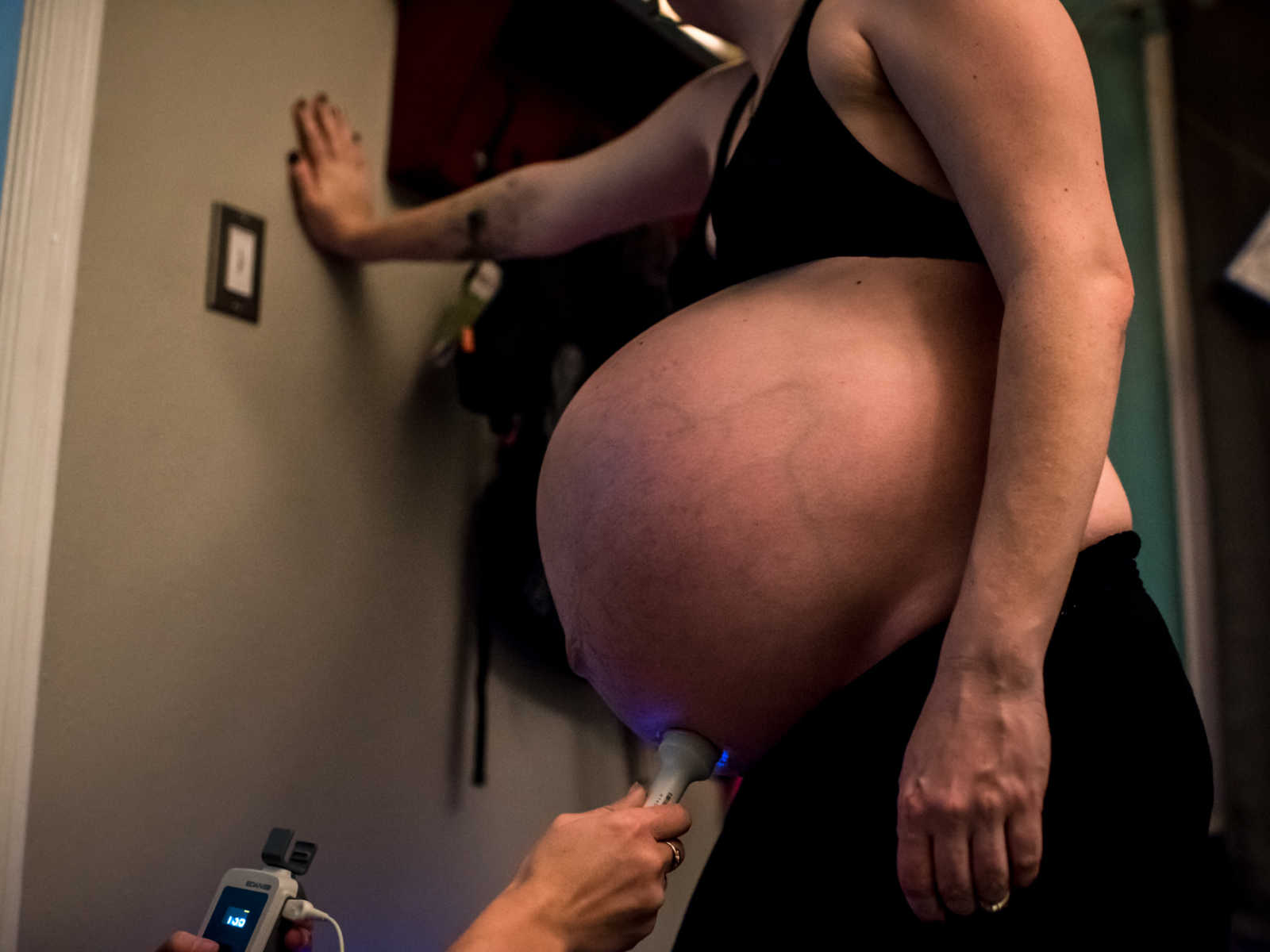 Pregnant woman standing in sports bra leaning against a wall before giving birth to 11 pound baby