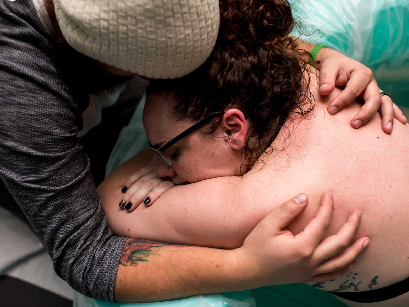 Pregnant woman leaning over side of birthing pool in pain being held by husband