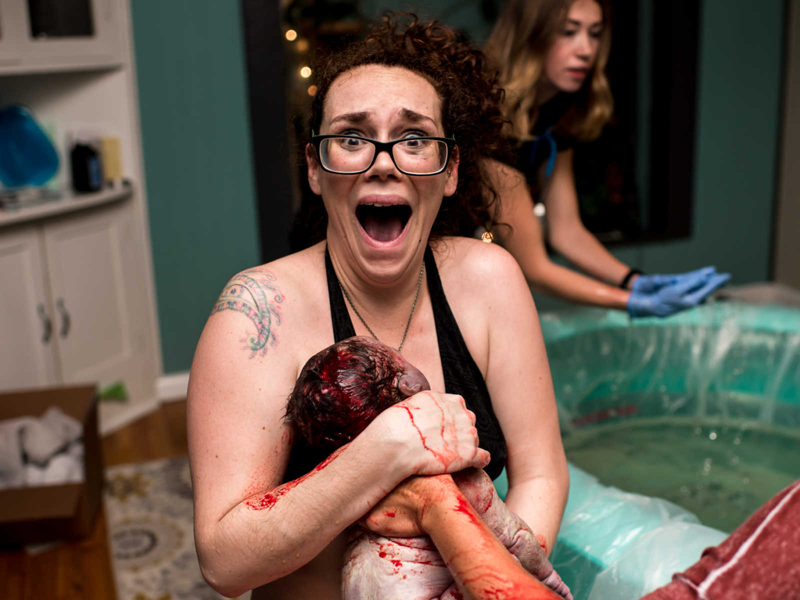 Woman holds bloody 11 pound newborn out side of birthing pool in look of shock
