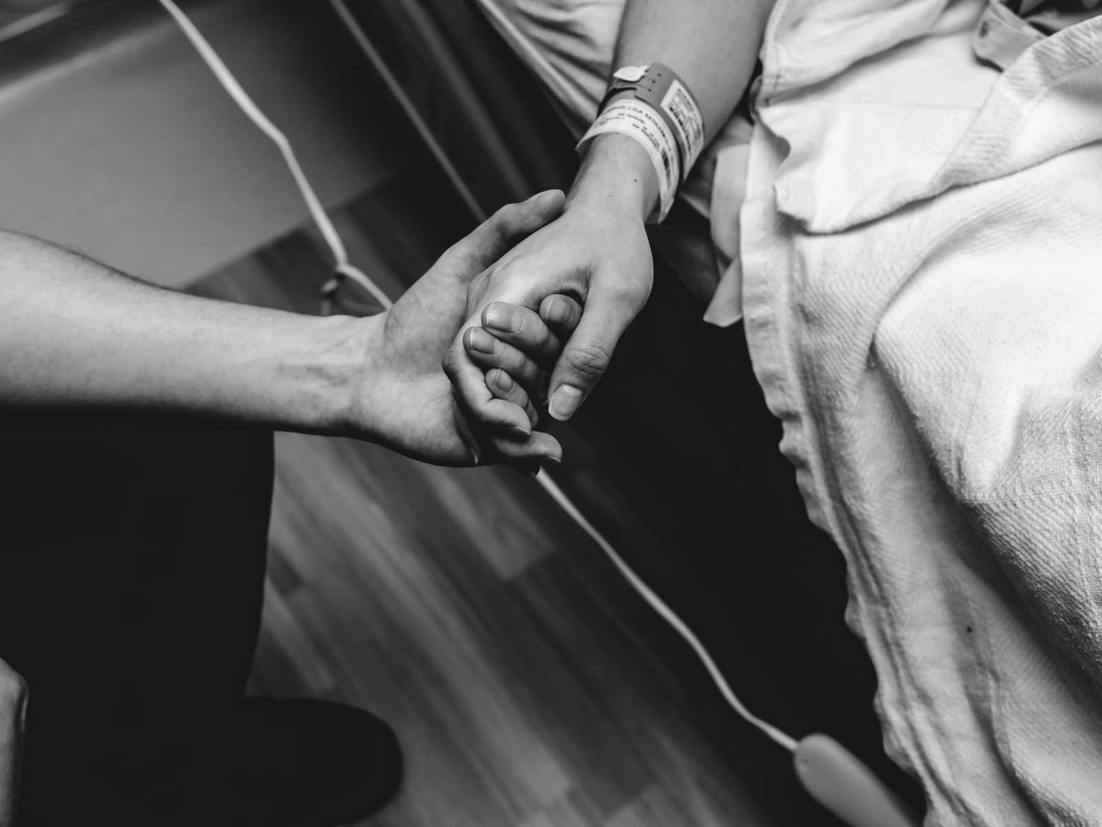 hands held on side of hospital bed and pregnant women's wrist has hospital bracelets 
