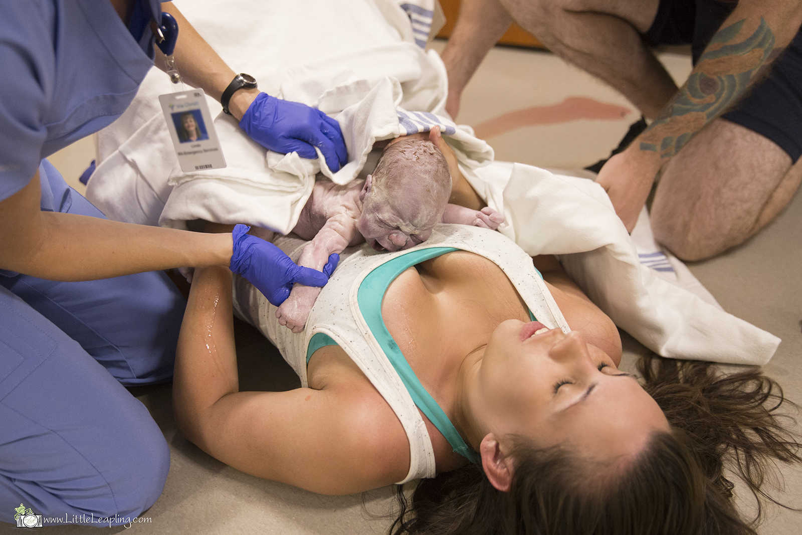 woman lies on the floor with newborn on her chest while nurse cleans off the baby