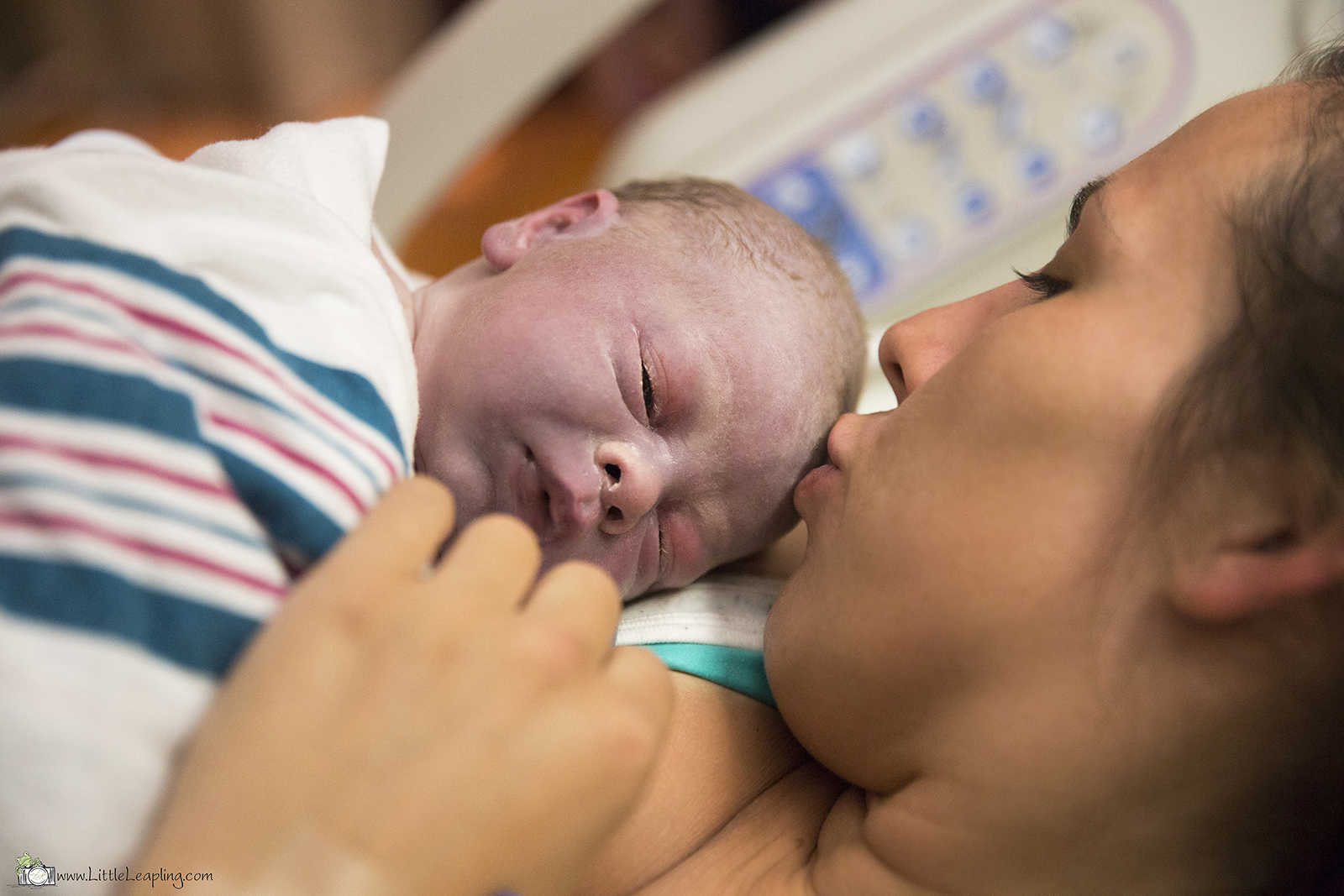 mother gives newborn baby a kiss on the forehead as it lies on her chest