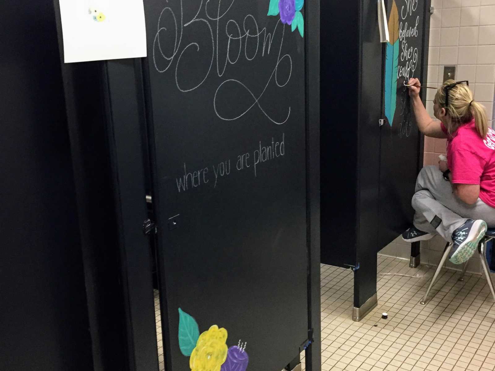 black bathroom stall with sketch of quote and woman sitting on stool to the right painting on another stall