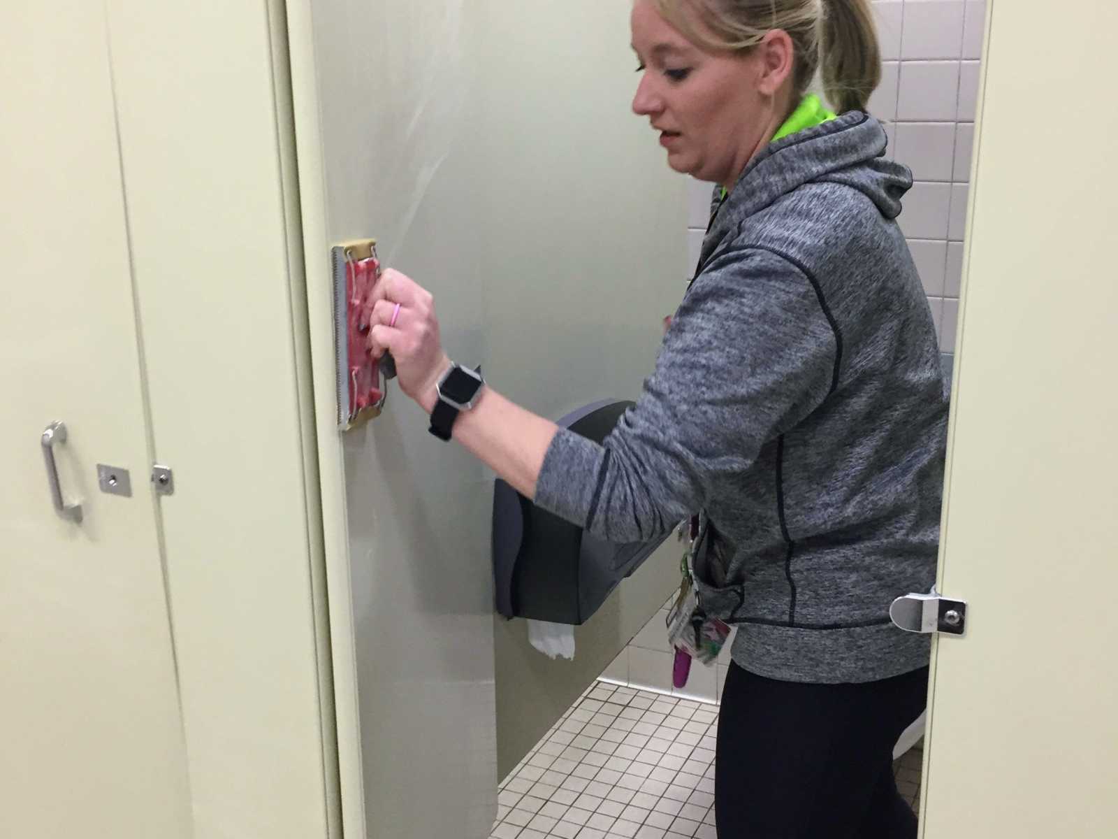 woman inside cream public bathroom stall sanding down door