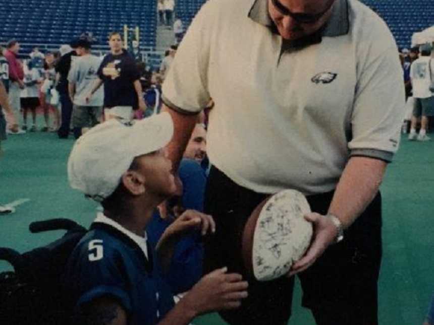 man with philadelphia eagles shirt hands autographed football to cerebral palsy teen in wheelchair