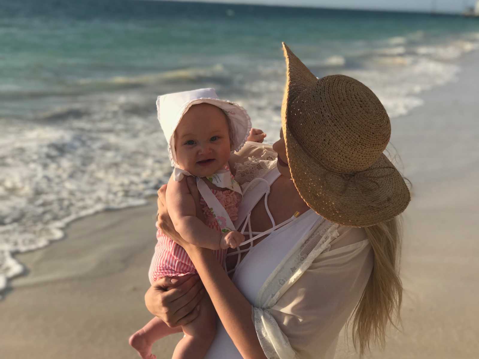 Mother with postpartum thyroid condition holds and looks at smiling baby near ocean shore