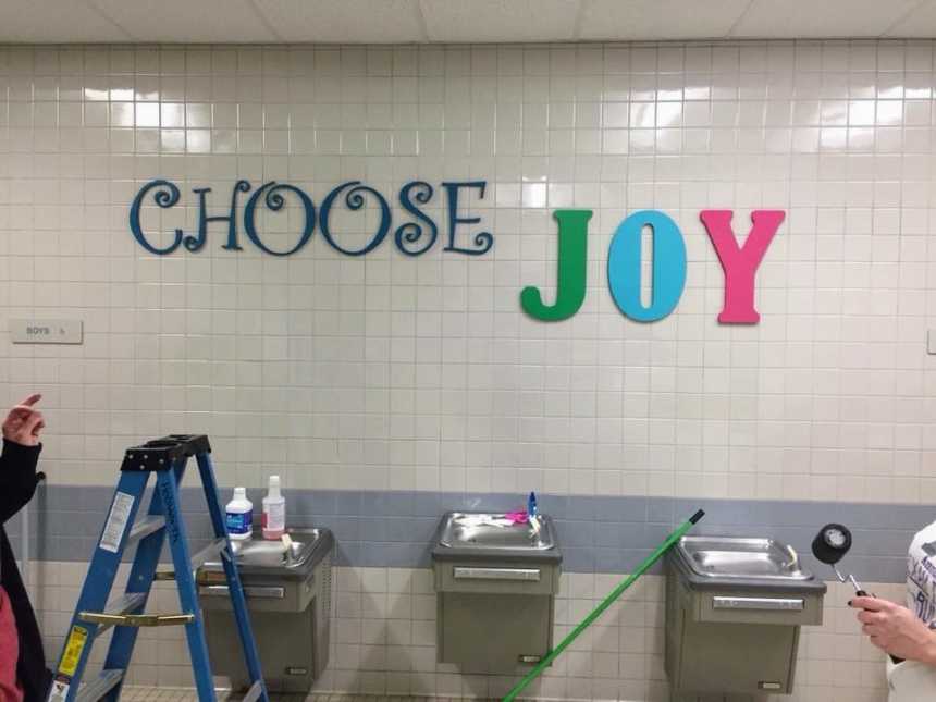 three public water fountains with supplies on them and blue latter to the left with large words above reading, "choose joy"