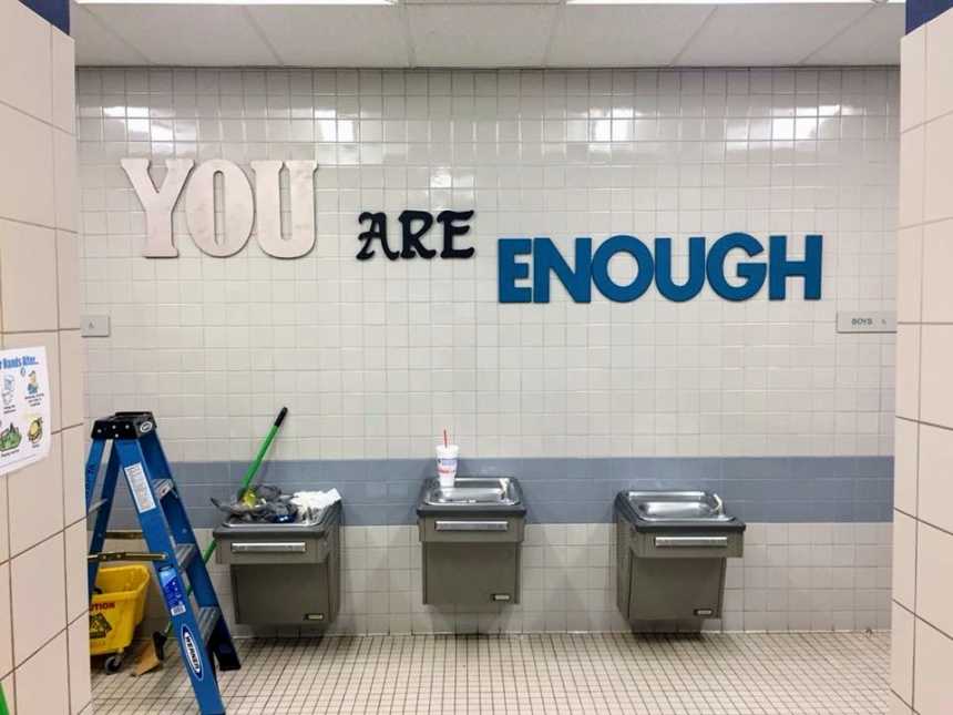 three public water fountains with a blue latter to the left of them and large words that read, "you are enough" above them