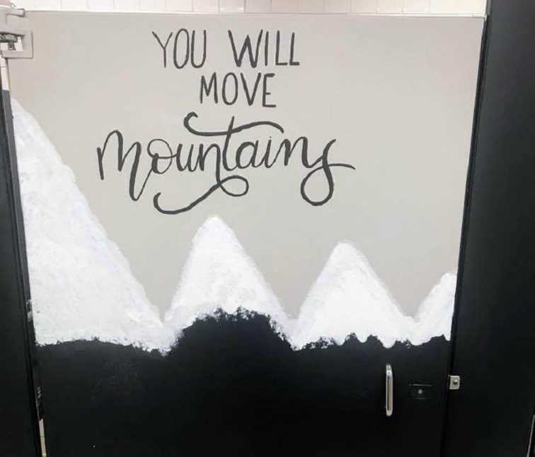 black bathroom stall door painted white at top with inspirational quote, "you will move mountains"