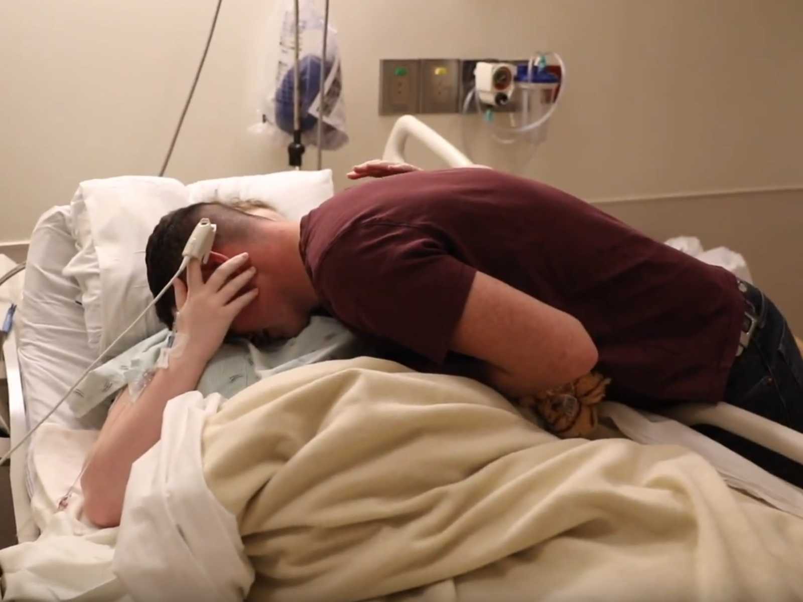 Husband leans over to hug wife in hospital bed who just gave birth via c-section