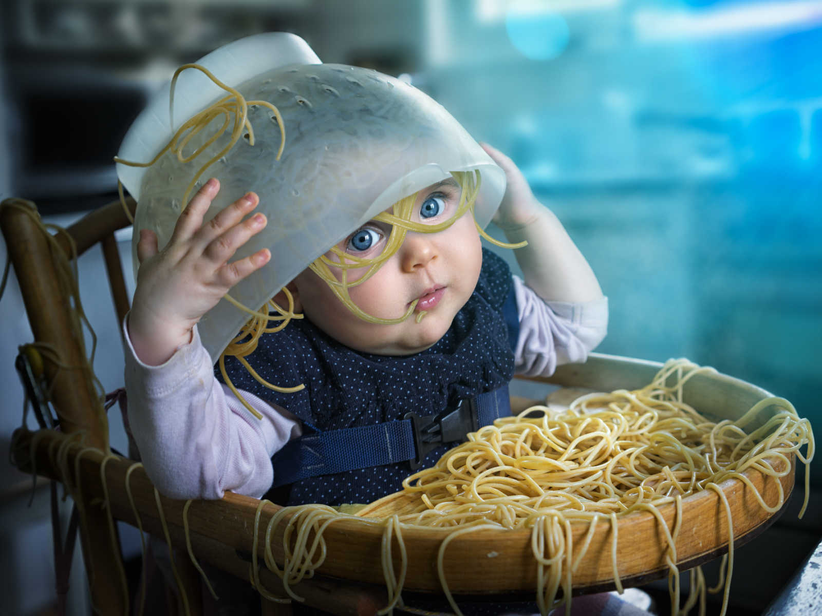 baby in high chair with animated strainer of noodles on top of her head with noodles shaped as glasses on her face