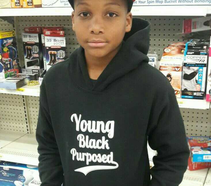 young teen with black sweatshirt on that says, "young black purposed" stands in in front of shelves at store