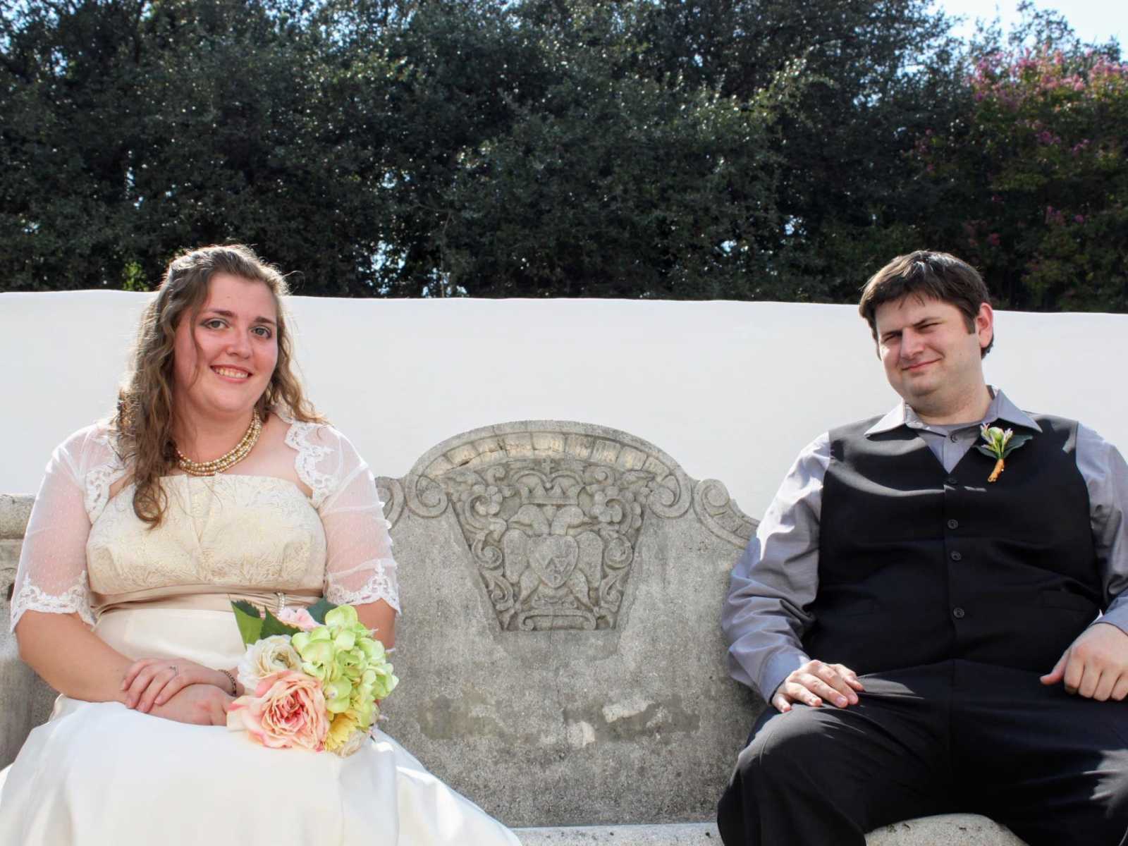 Bride and groom smile while sitting on stone bench