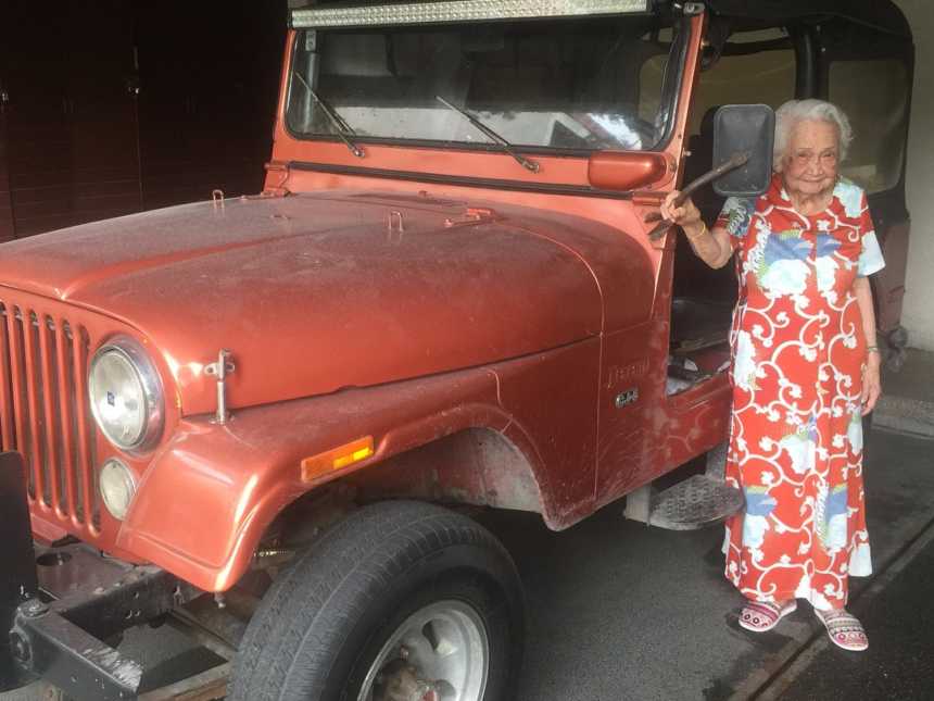 woman in a casual floor length dress standing next to an old doorless red jeep