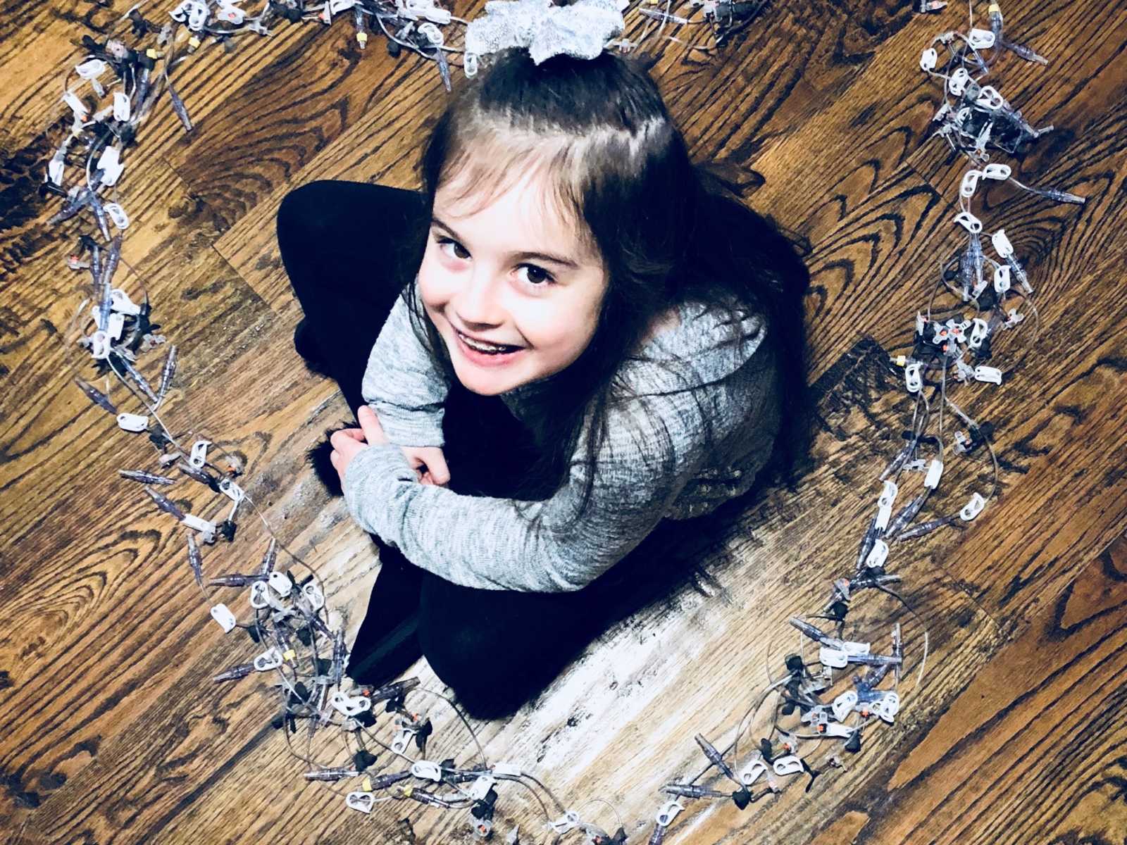 Little girl with rare disease looks up smiling while surrounded by needs in heart shape