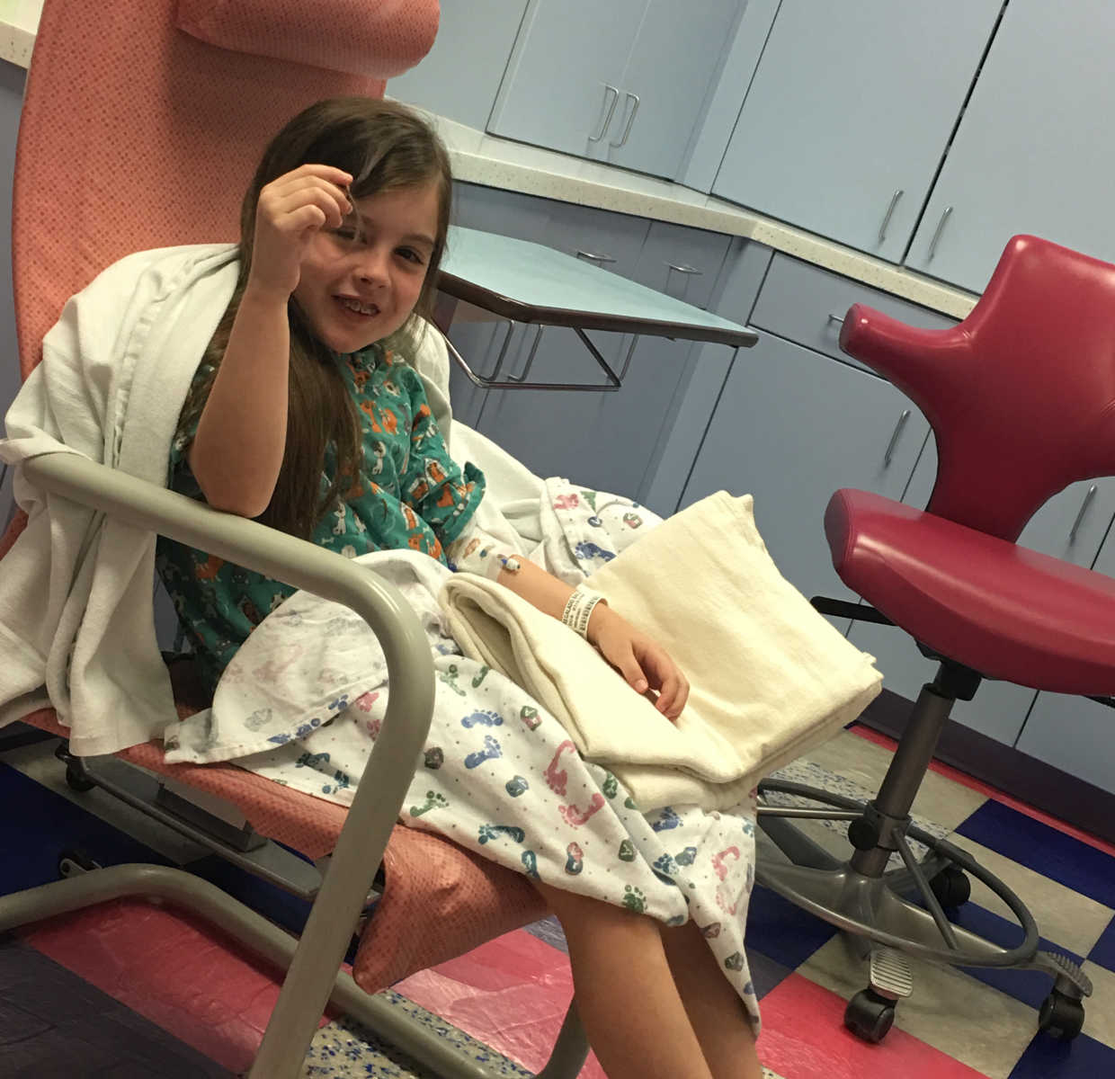Little girl with rare disease sits in hospital chair smiling with blankets on her
