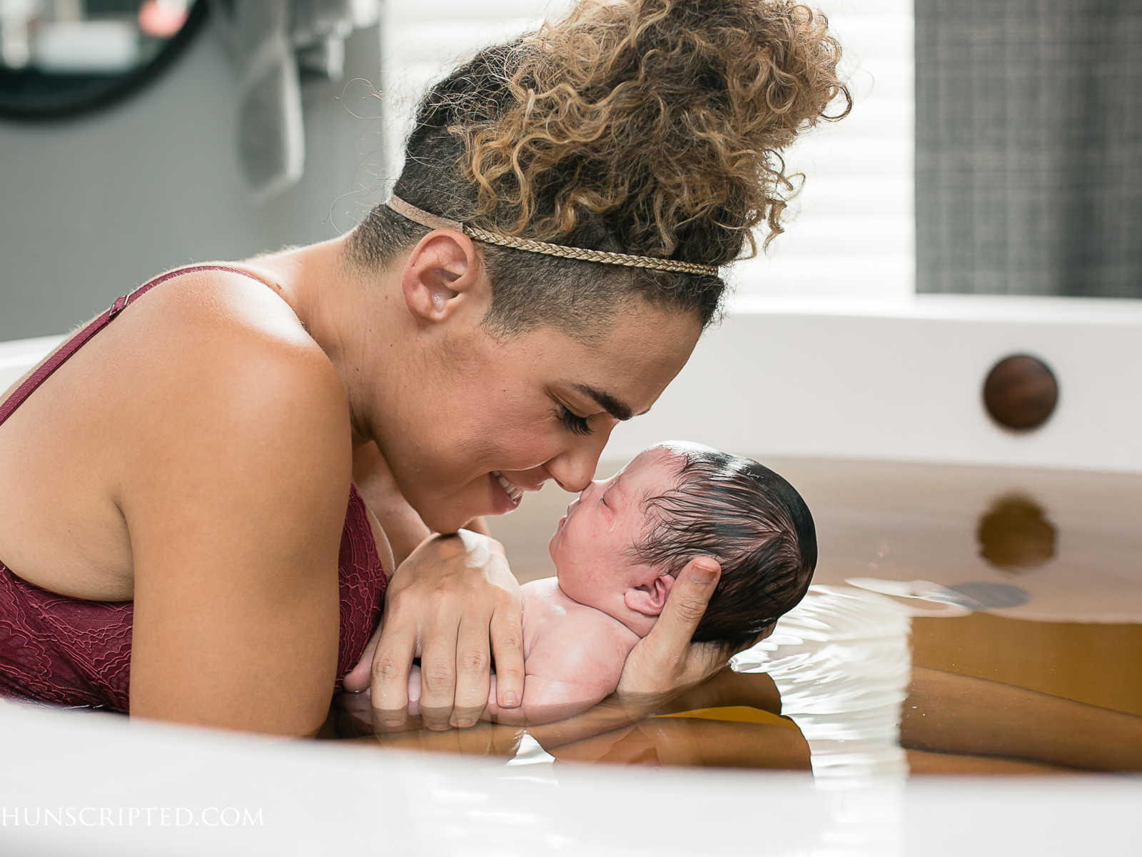 close up of mother nose to nose with newborn in white tub of murky water