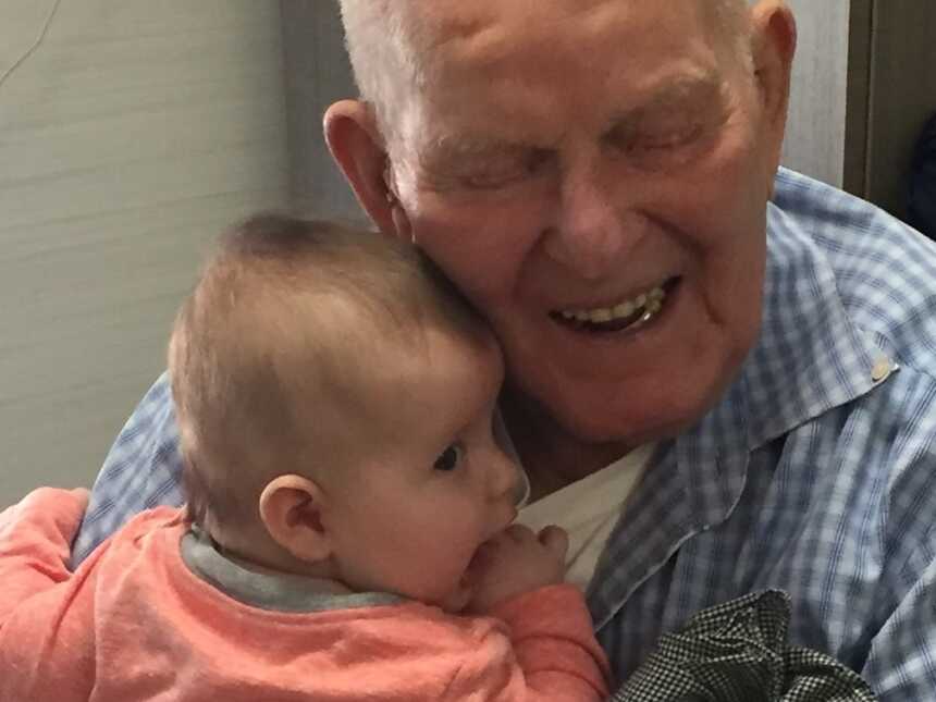 Great grandfather smiling while embracing newborn baby