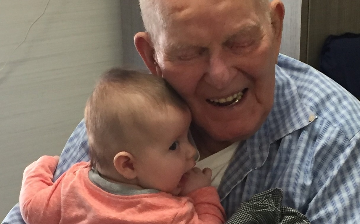 Great grandfather smiling while embracing newborn baby