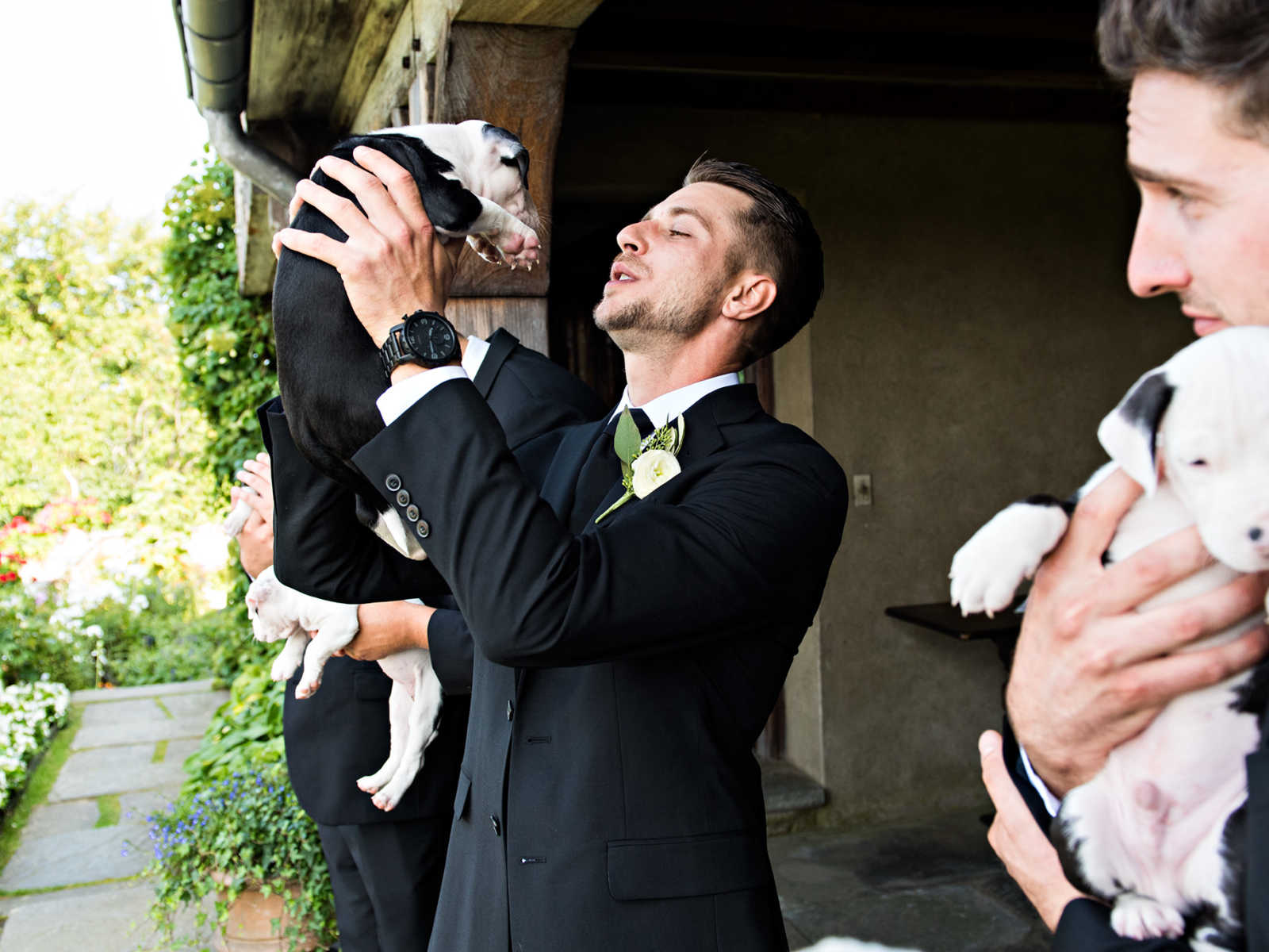 Groomsman holds up rescue puppy in the air so they are eye to eye