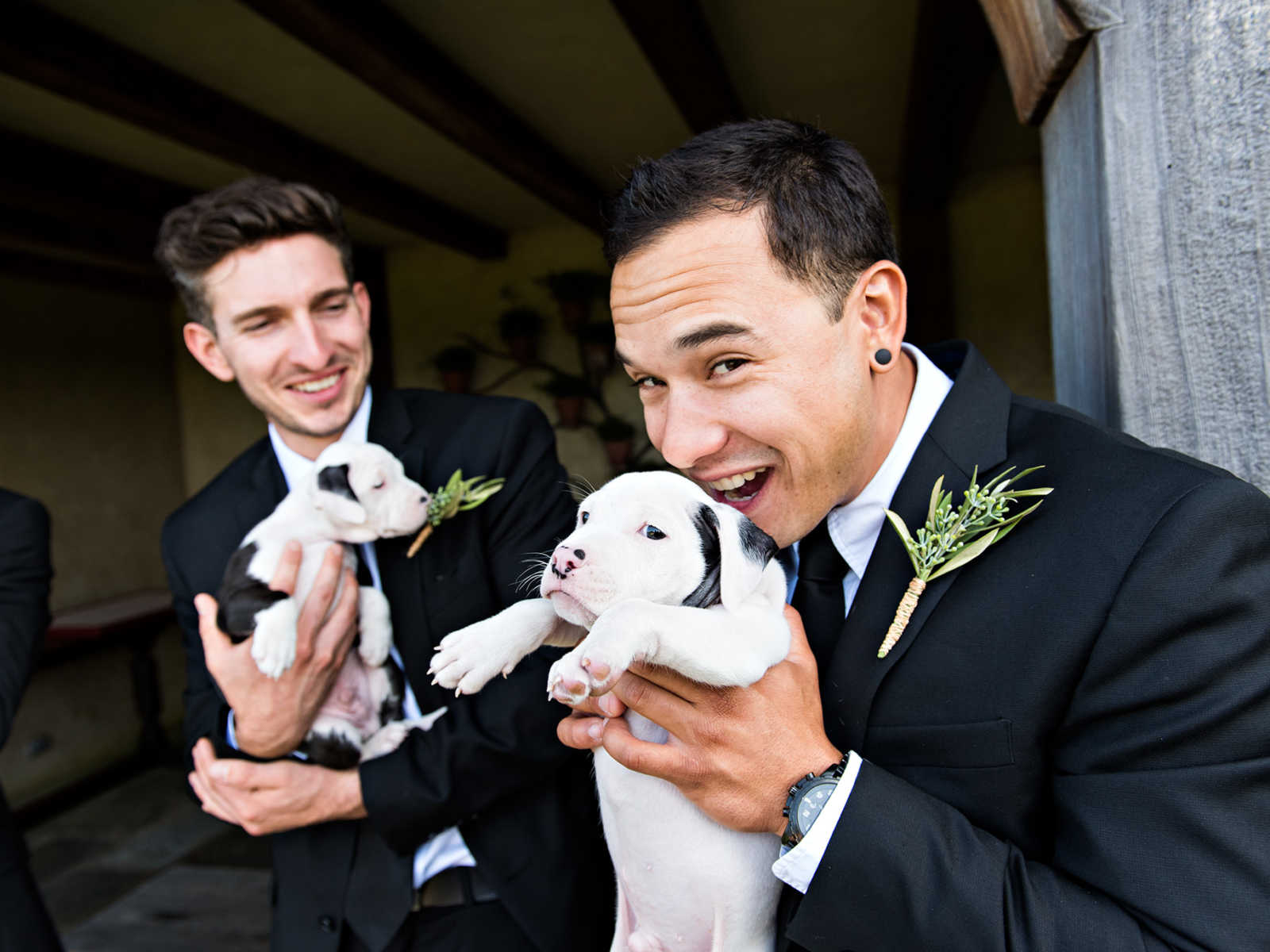 Groomsmen laugh as they both hold rescue puppies
