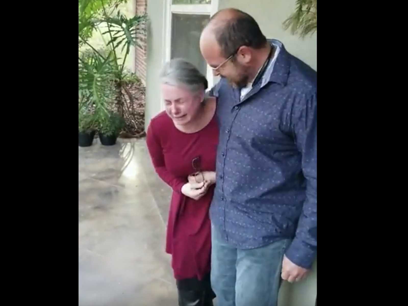 Man holds his arm around woman as she cries