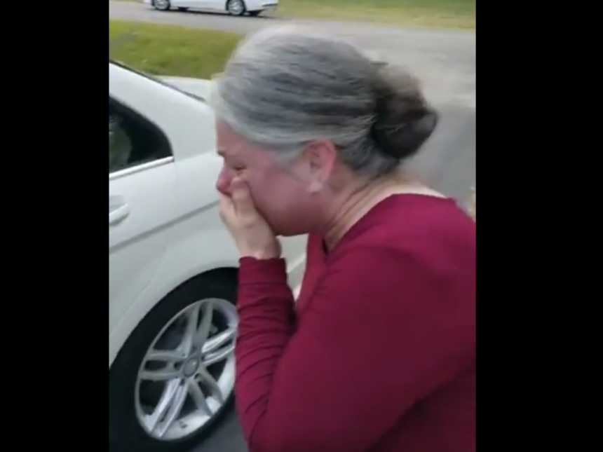 Woman cries with hand over her mouth in front of brand new white Mercedes