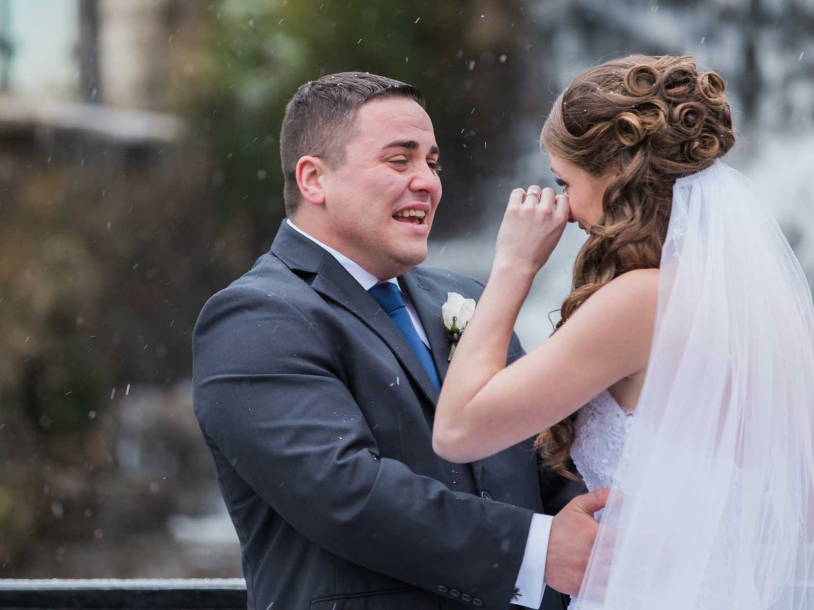 groom holds bride as she wipes away a tear