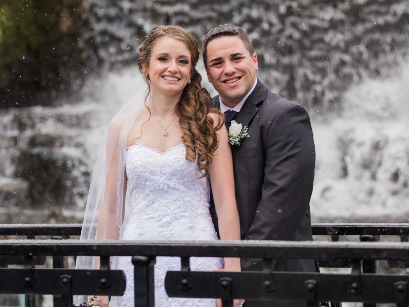 bride and groom hand in hand smiling in front of waterfall as snow falls