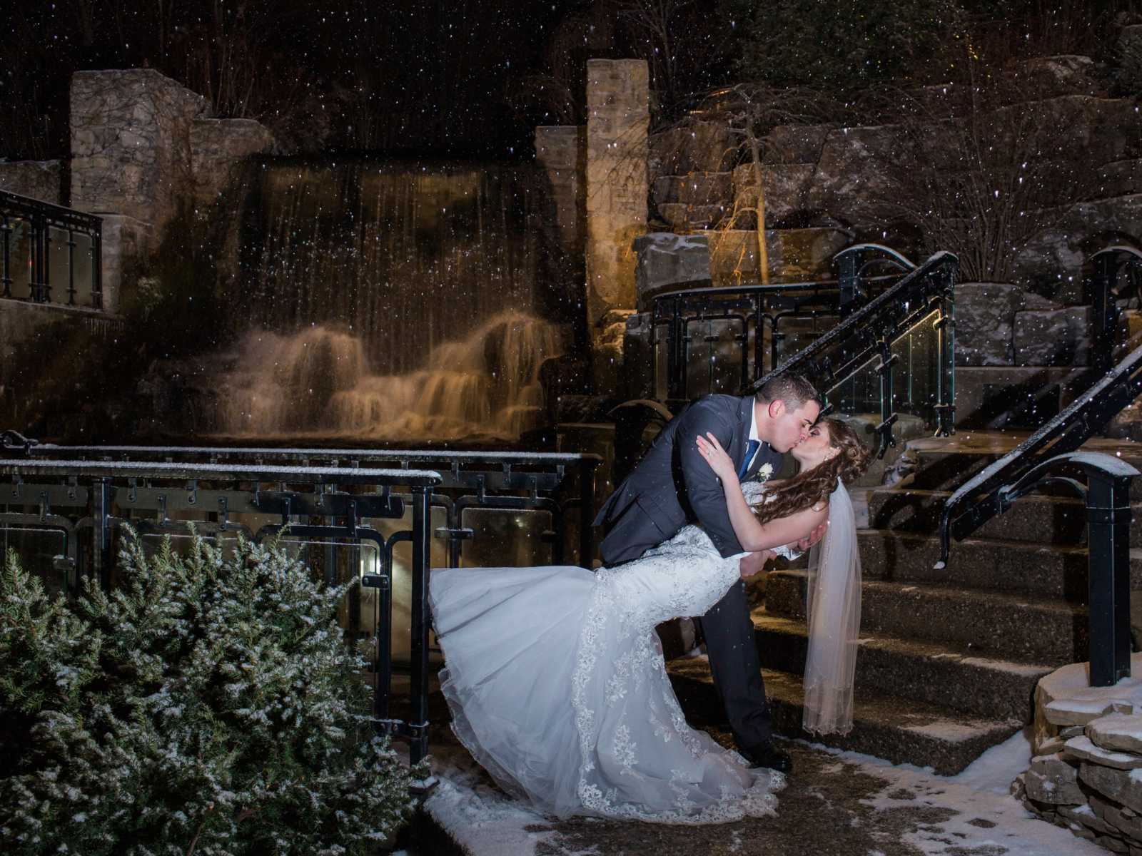 groom dips the bride in a kiss under the moonlight in front of waterfall