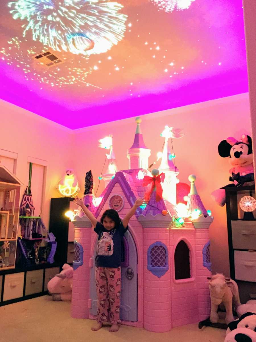 Little girl stands in front of Disney castle in her room with fireworks on ceiling