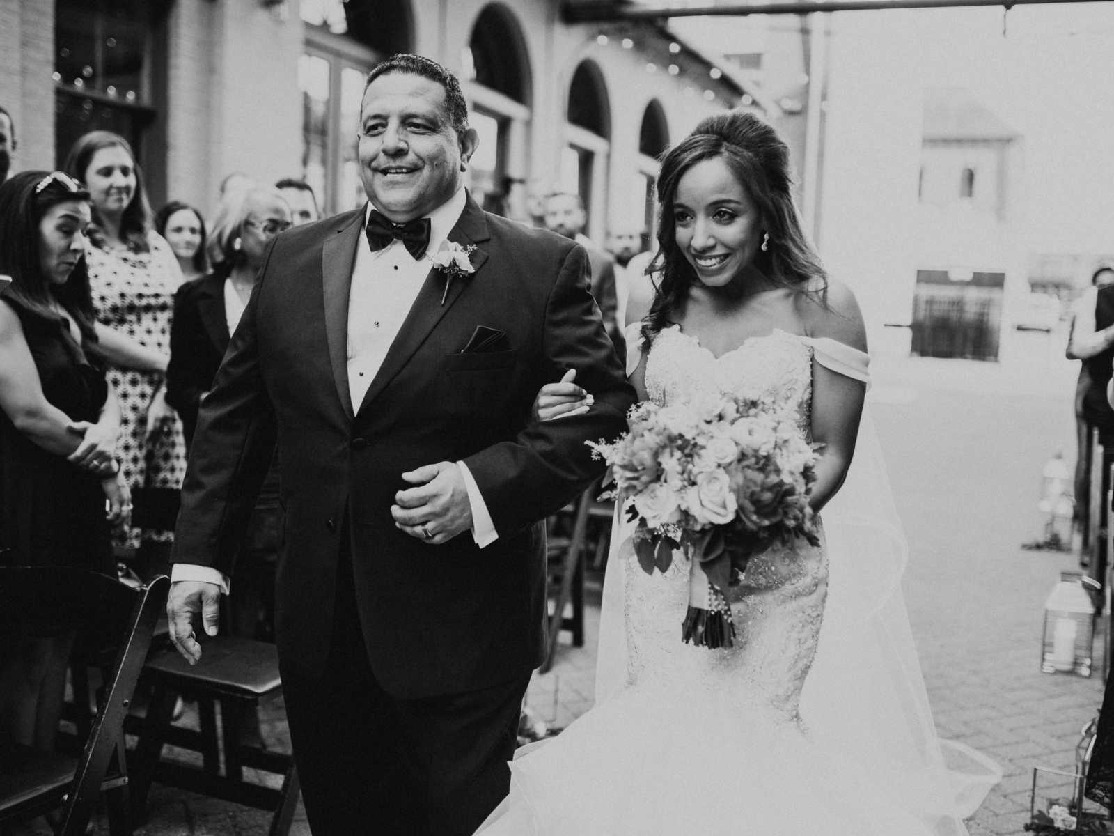 Bride and father smile as they walk down the aisle at daughter's wedding