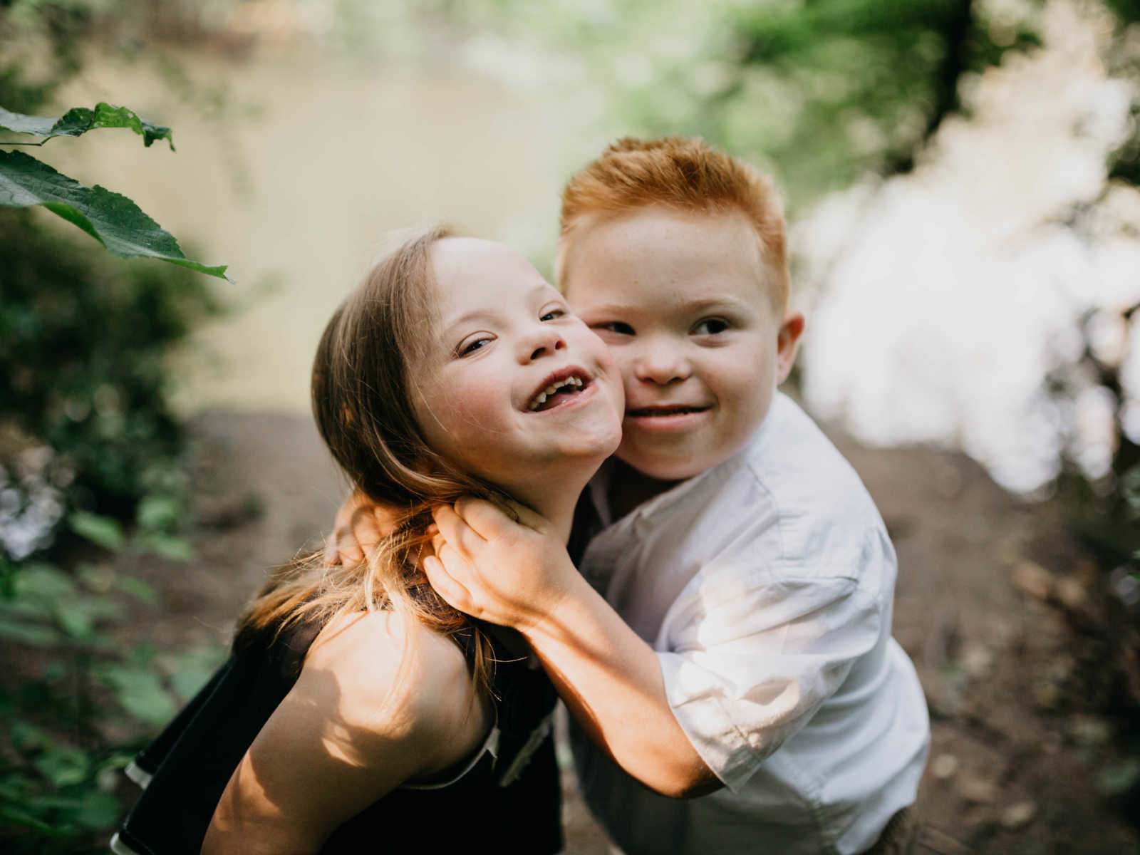 Down syndrome boy and girl smiling while boy has his arms around girl