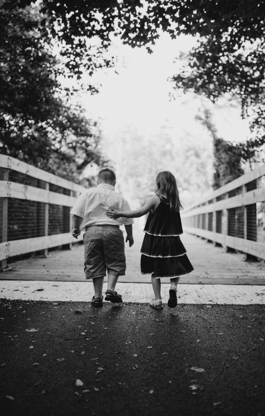 View from the back of down syndrome boy and girl walking on bridge