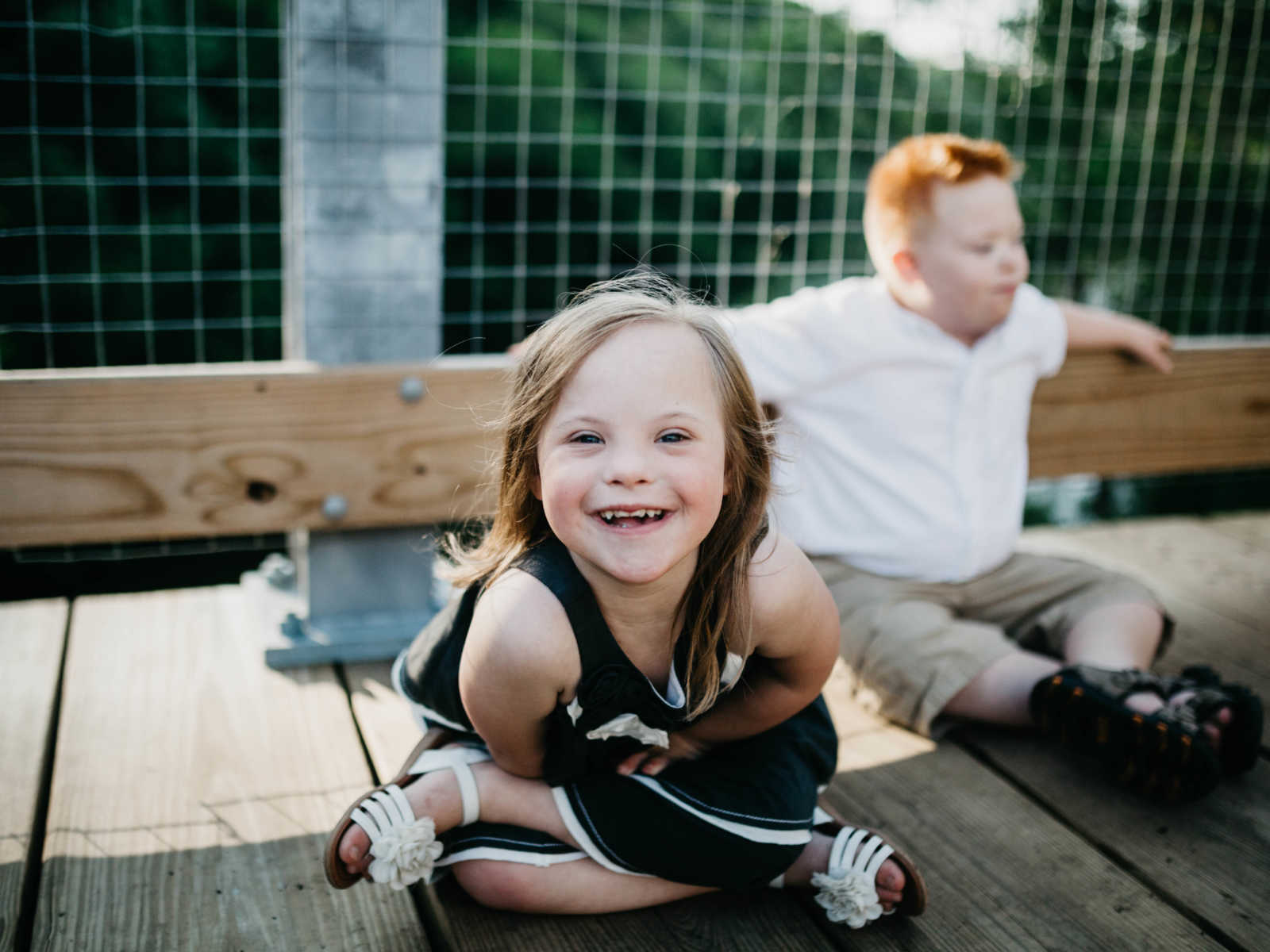 Down syndrome girl smiling while sitting next to down syndrome boy who is leaning on bridge